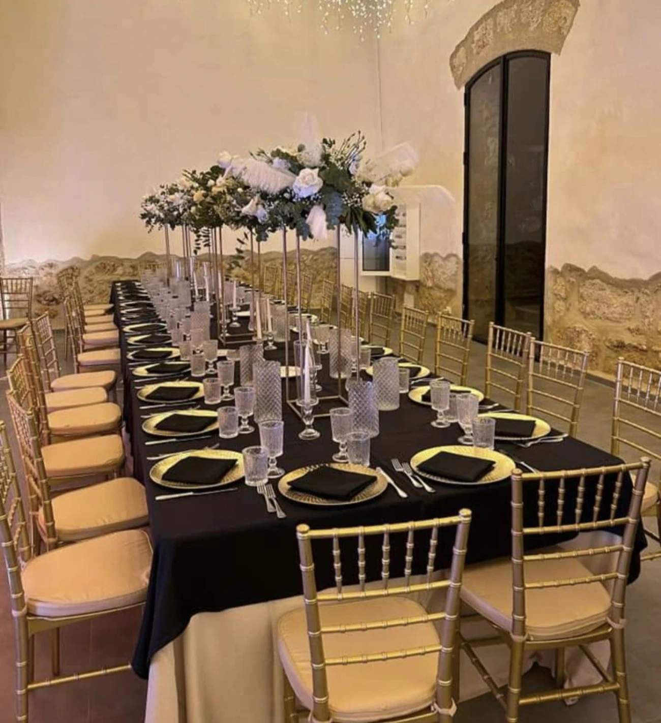 Tavolo nero con sedie dorate e alzate di fiori bianchi, nella sala in pietra